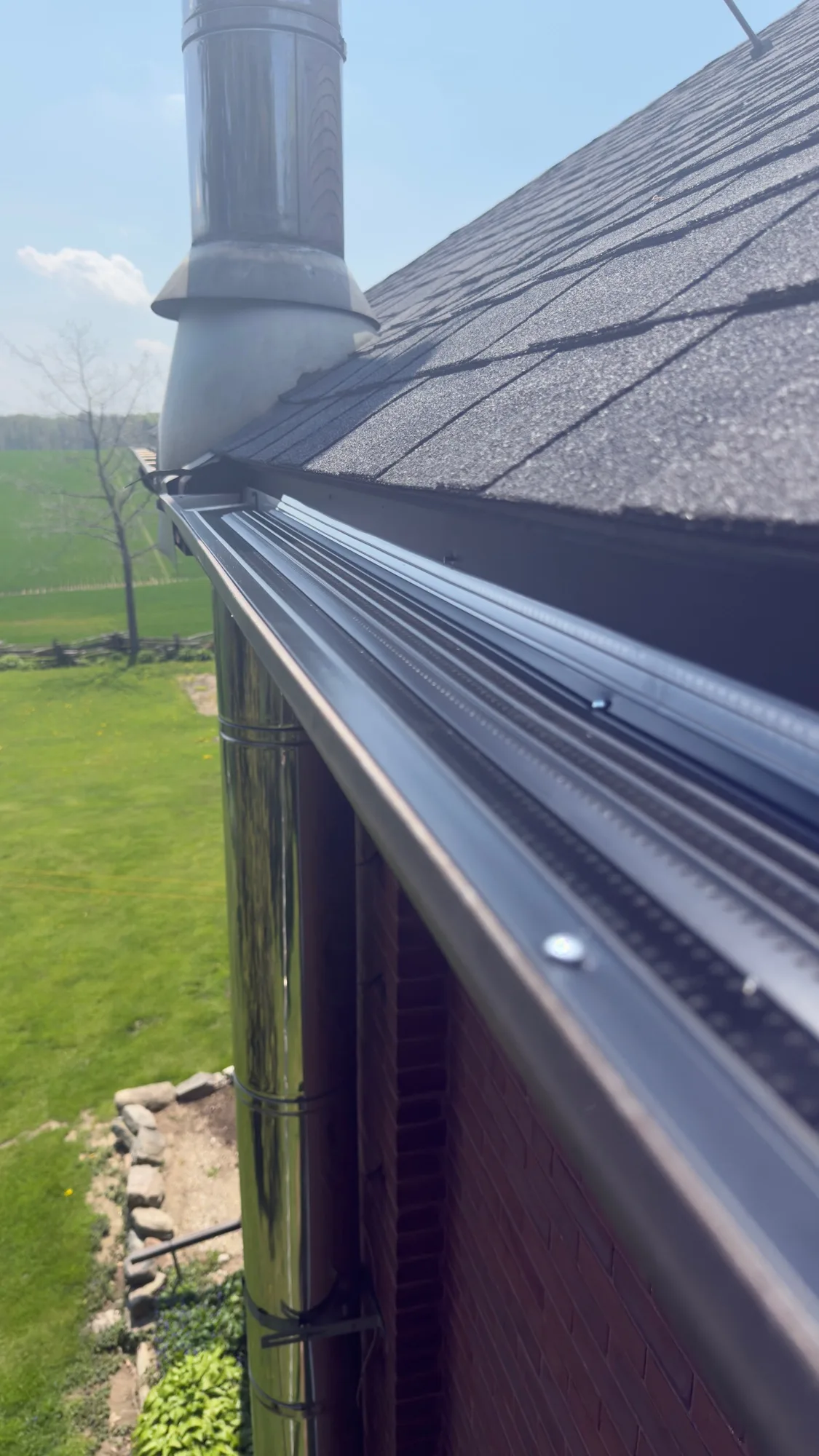 Black gutter guard installed on red brick rural home with farmland view — D&D Home Services