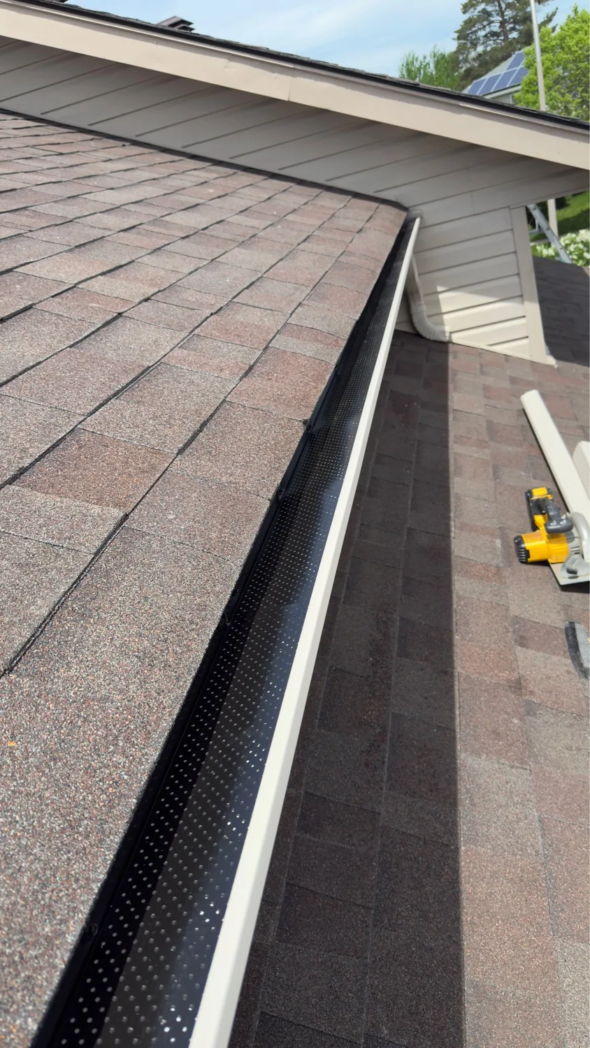 Close-up of installed black perforated gutter guard against red-brown asphalt shingles — D&D Home Services