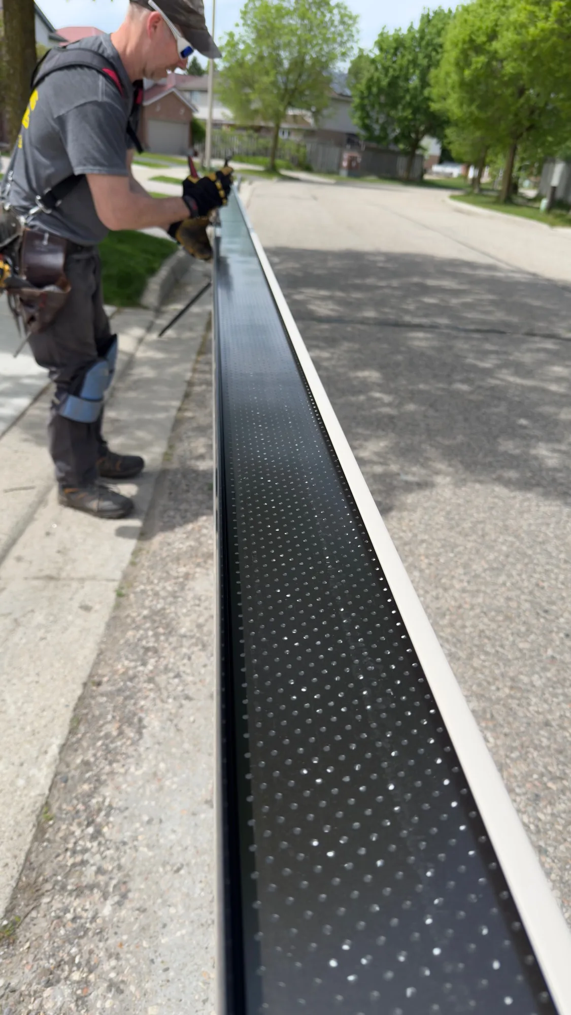 Long perspective view of perforated black gutter guard section being prepared for install — D&D Home Services
