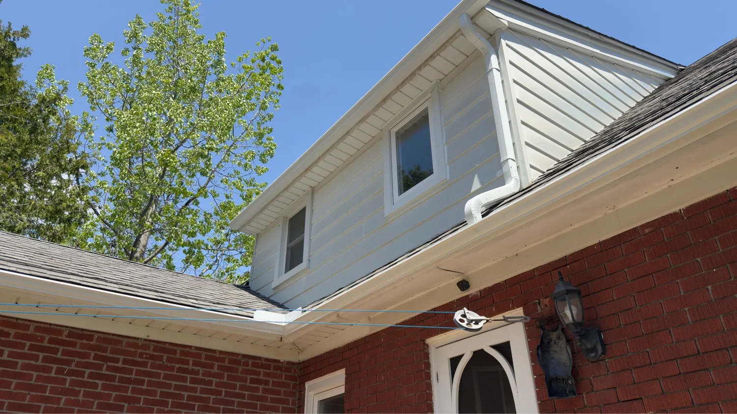 White seamless eavestrough with downspout on red brick two-storey home — D&D Home Services