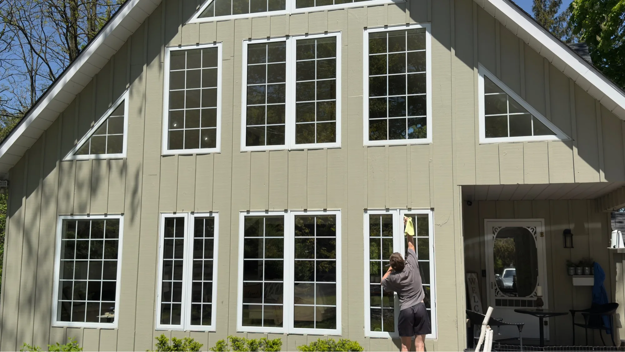 D&D Home Services technician hand-cleaning windows on tall sage A-frame home with full picture windows in Kitchener-Waterloo
